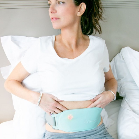 Femme utilisant une ceinture chauffante pour soulager naturellement les douleurs menstruelles à la maison